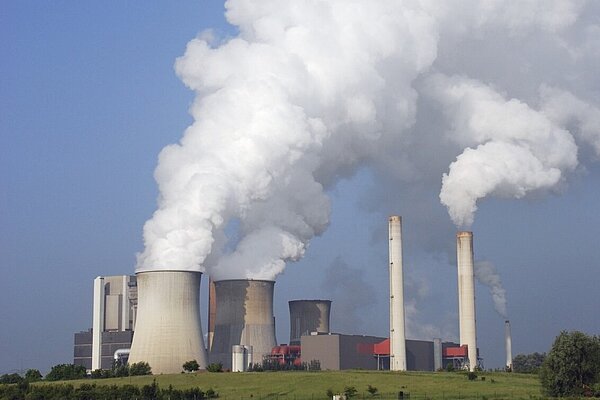 A power station with smoke blowing out of the chimneys.